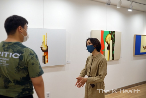 강윤정 작가(오른쪽)가 유디갤러리를 찾은 관람객에게 작품을 설명하는 모습(사진제공 : 유디치과)